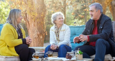 three friends seated around a low table outside, chatting, smiling, drinking tea